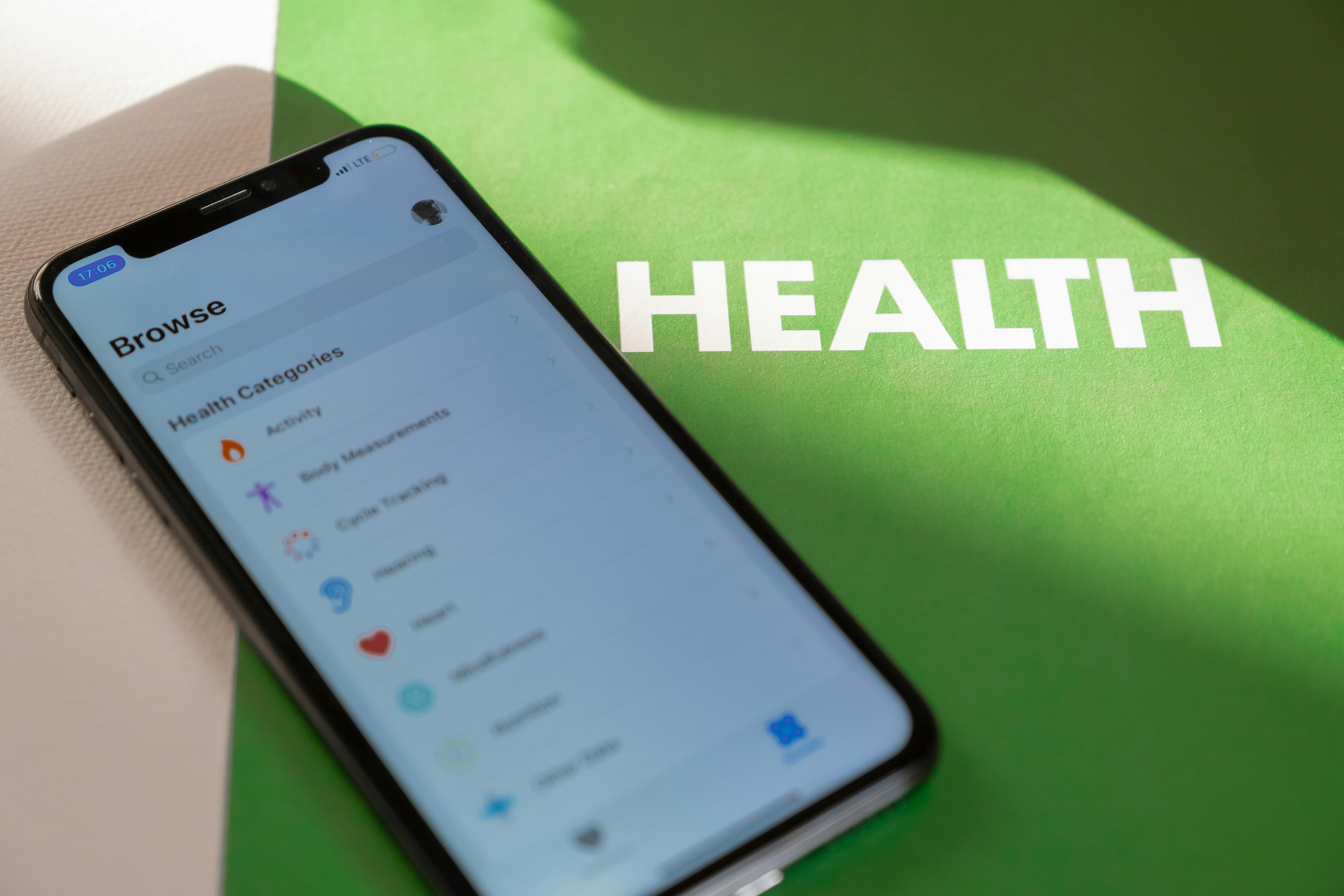 A smartphone displaying a 'Health' app with various tracking categories, resting on a bright green surface with the word 'HEALTH' printed in bold white letters.